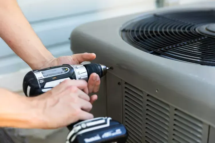 A person is using a drill to fix an air conditioner.