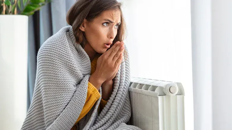 A woman wrapped in a blanket is sitting in front of a heater.