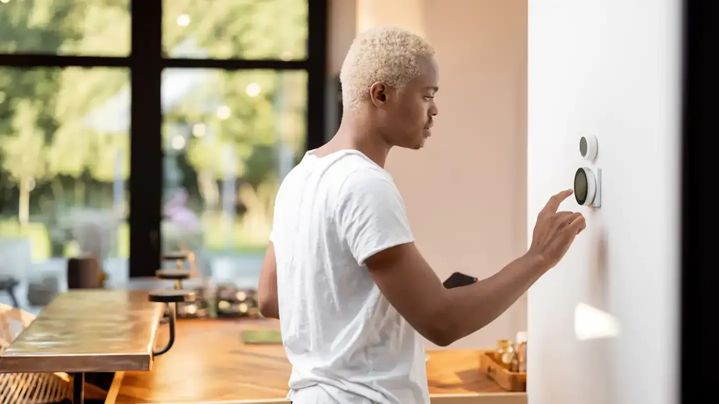 A man is adjusting a thermostat in a kitchen.