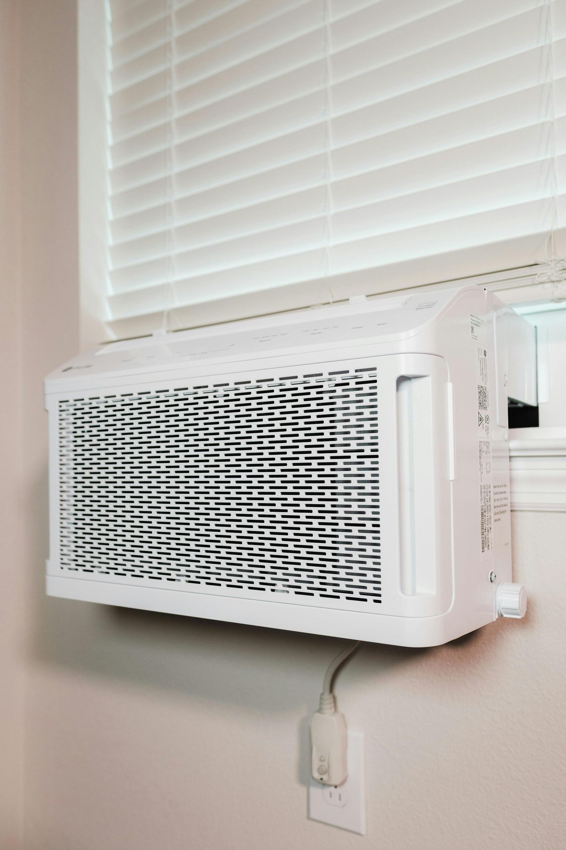 A white air conditioner is hanging on a wall next to a window.