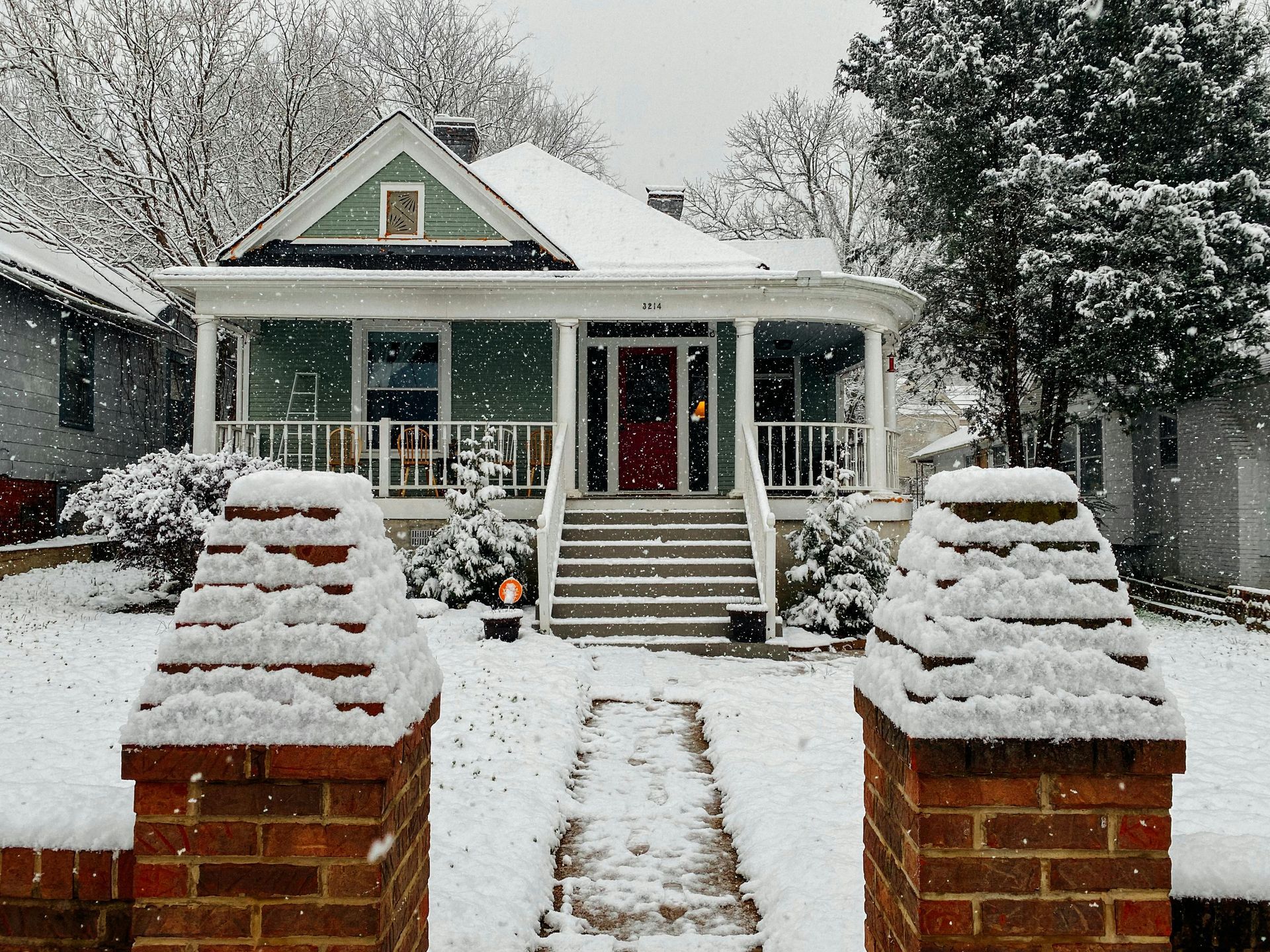 A green house with a red door is covered in snow.