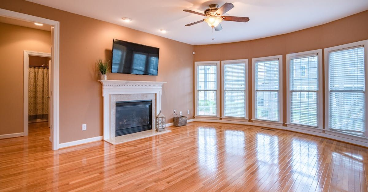 An empty living room with hardwood floors , a fireplace , a flat screen tv and a ceiling fan.