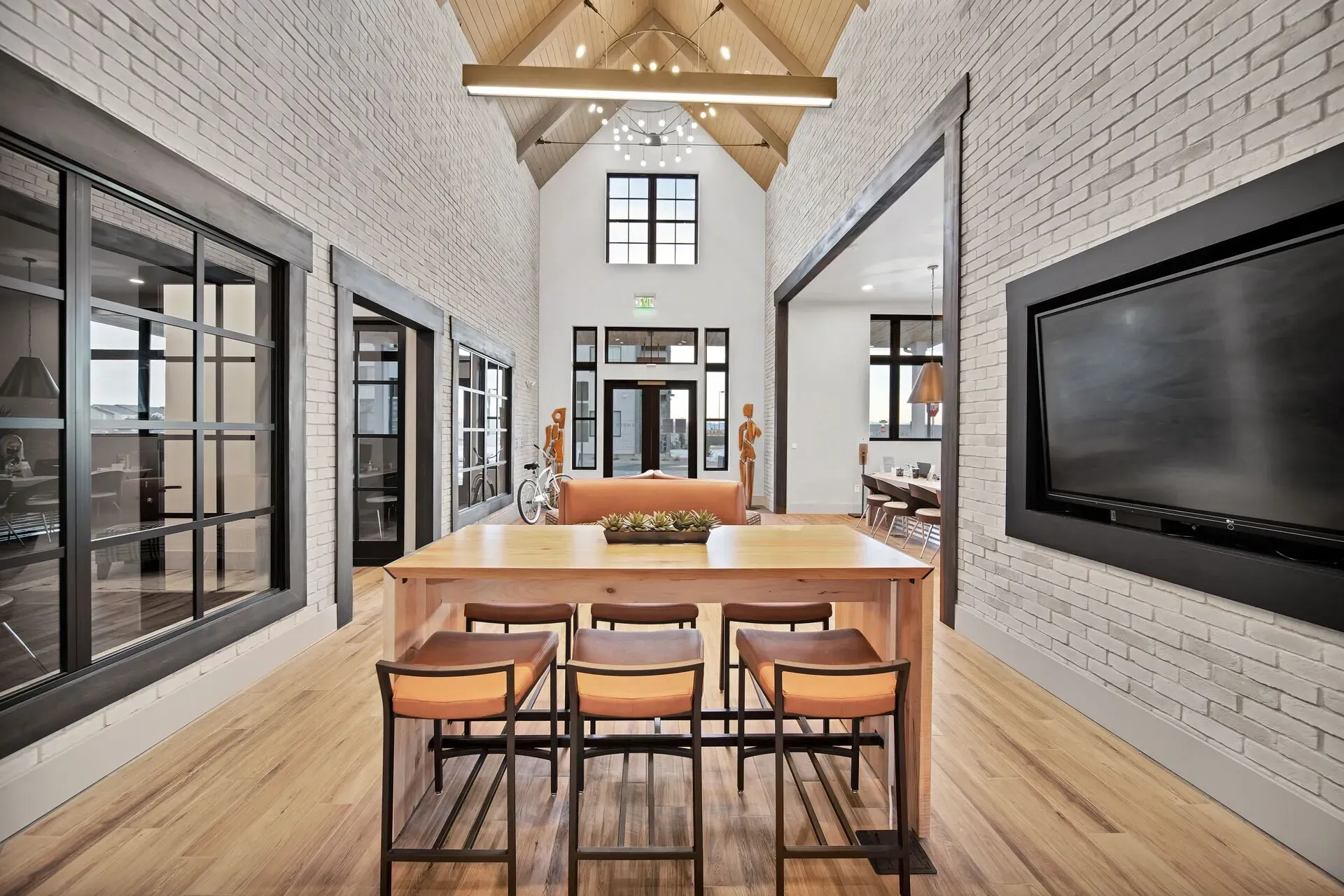 Modern communal lounge with a large wooden table, bar stools, and a TV.