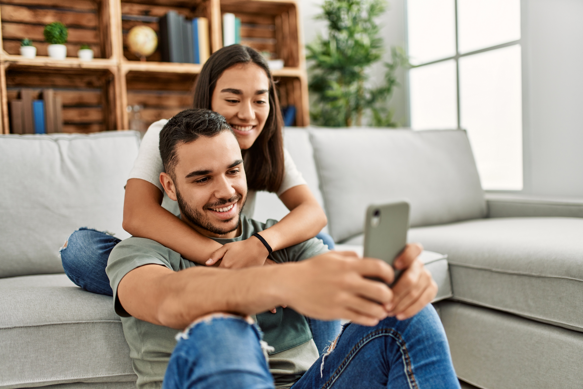 Smiling couple on a couch taking a selfie on a smartphone in a bright living room
