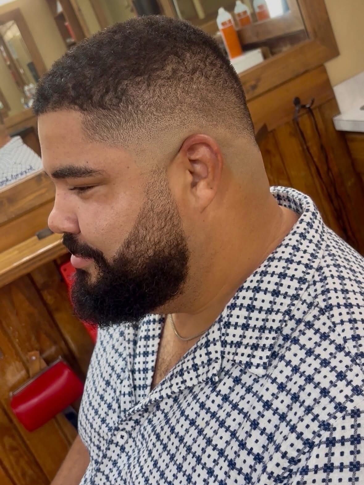 Man with fade haircut and beard, wearing a patterned shirt, indoors.