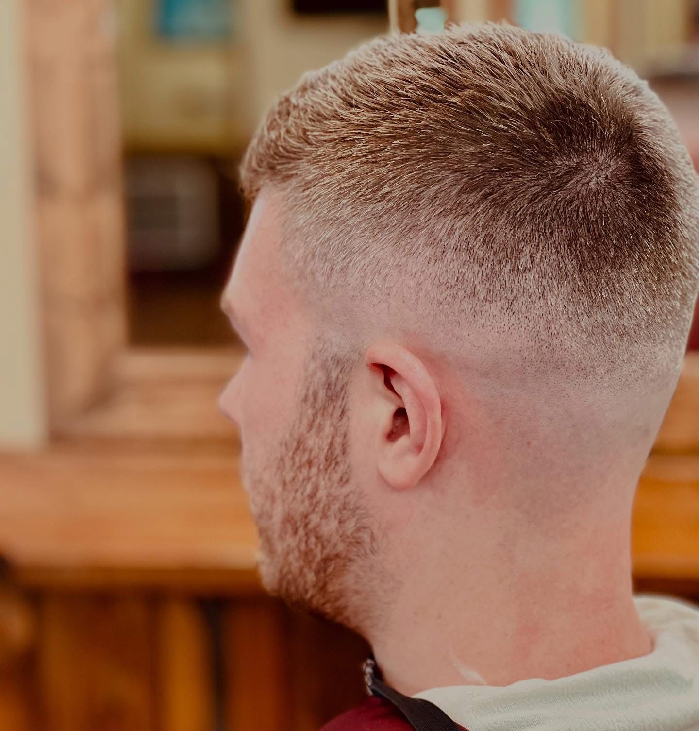 Man with short, faded blonde hair, side profile. Near wood surface.