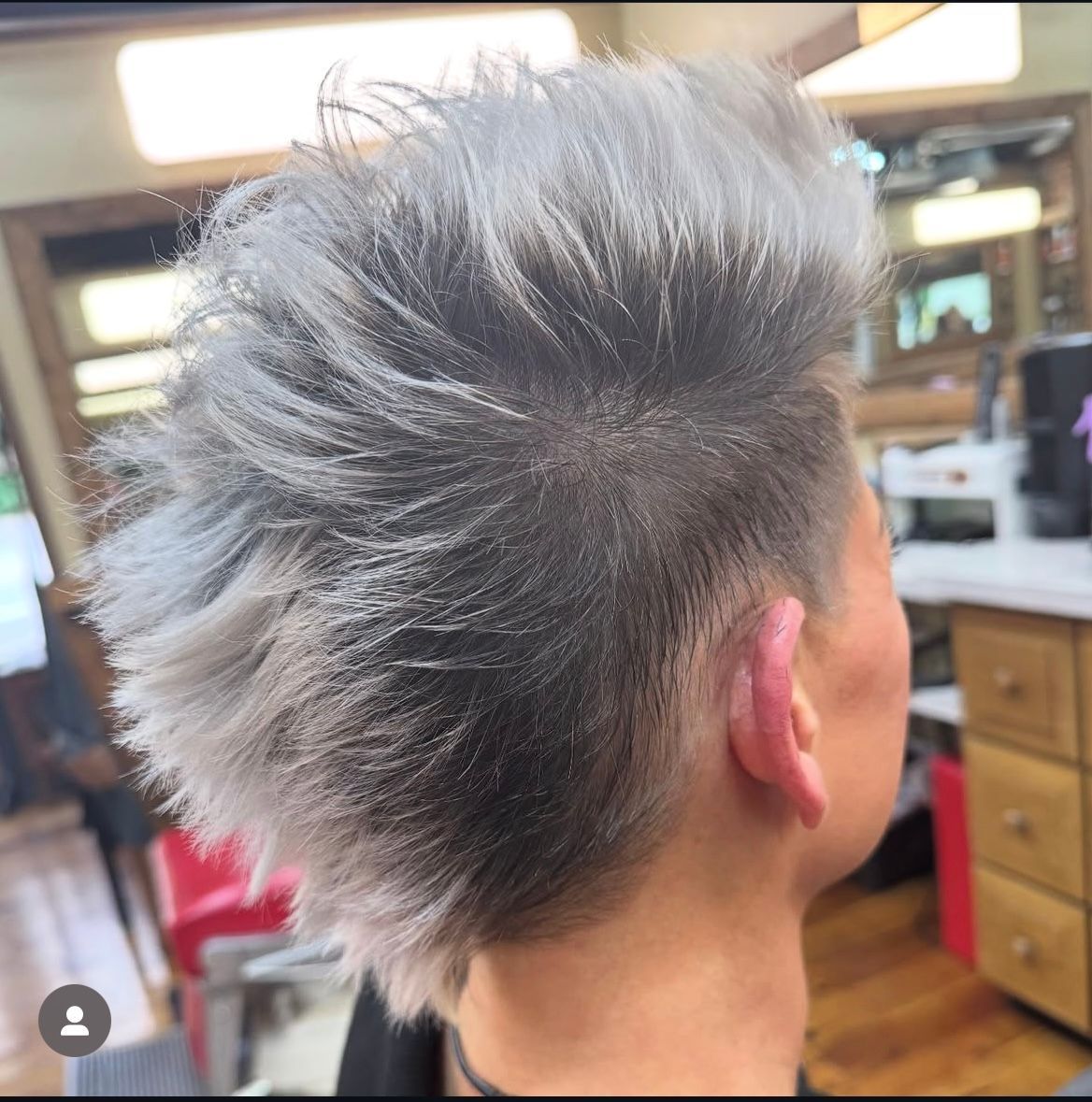Person with spiky, gray hair and shaved sides, in a hair salon.