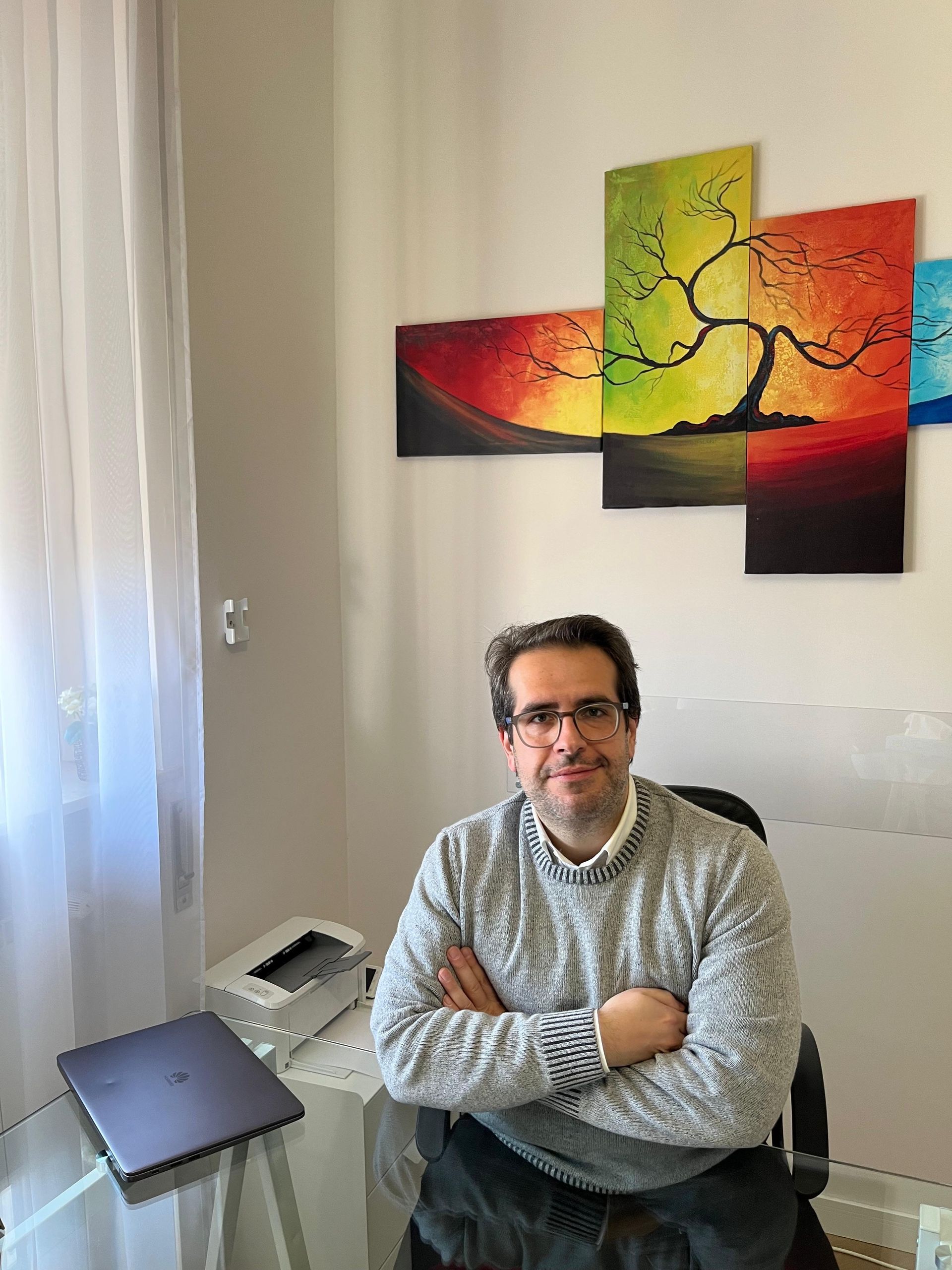 In una sala trattamenti, una persona sorridente in camice bianco è seduta su un lettino da massaggio, con in mano un metro a nastro rosa.