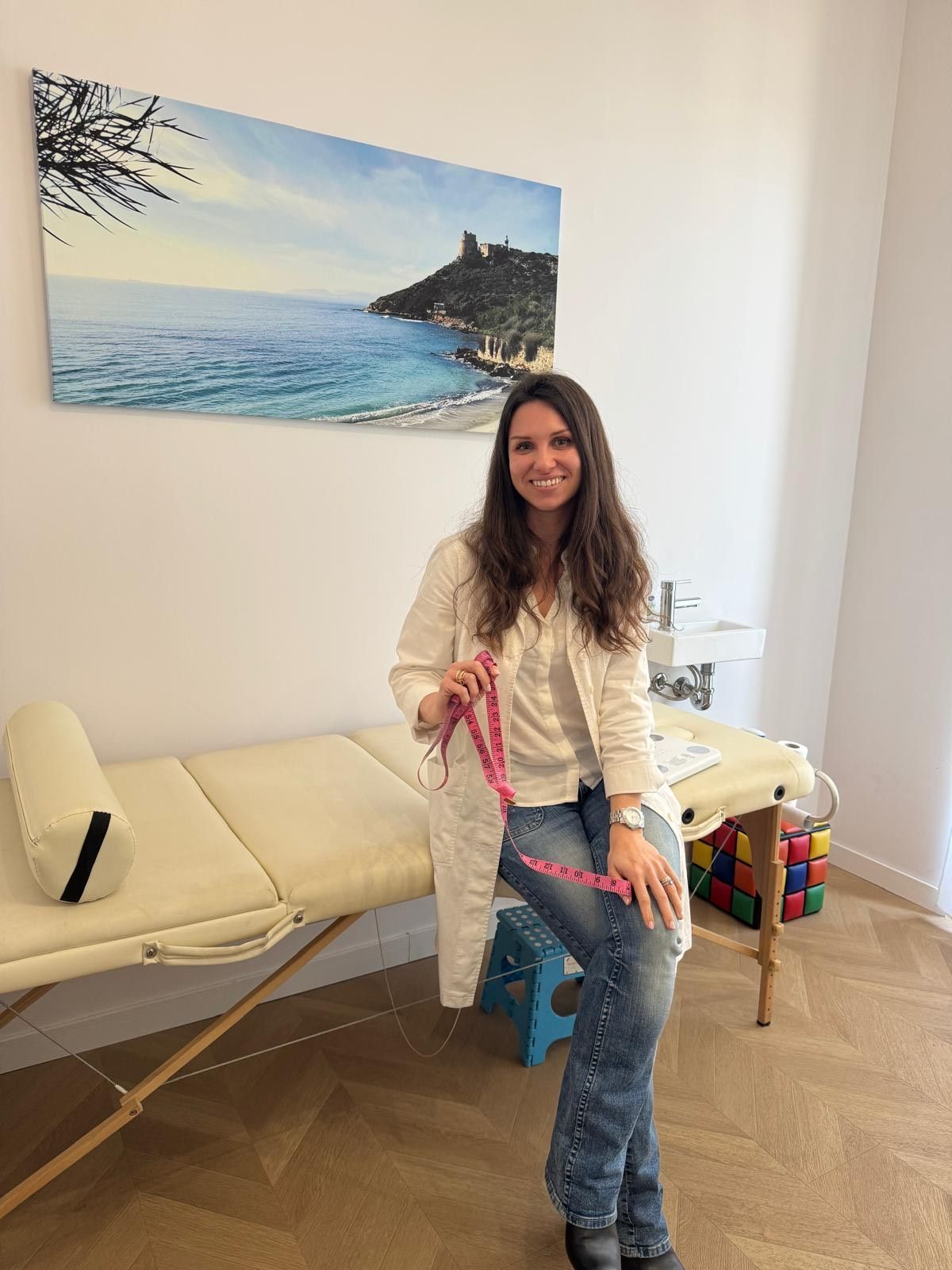 Un uomo con i capelli corti e la barba, che indossa un maglione grigio, posa davanti a una libreria bianca piena di libri.