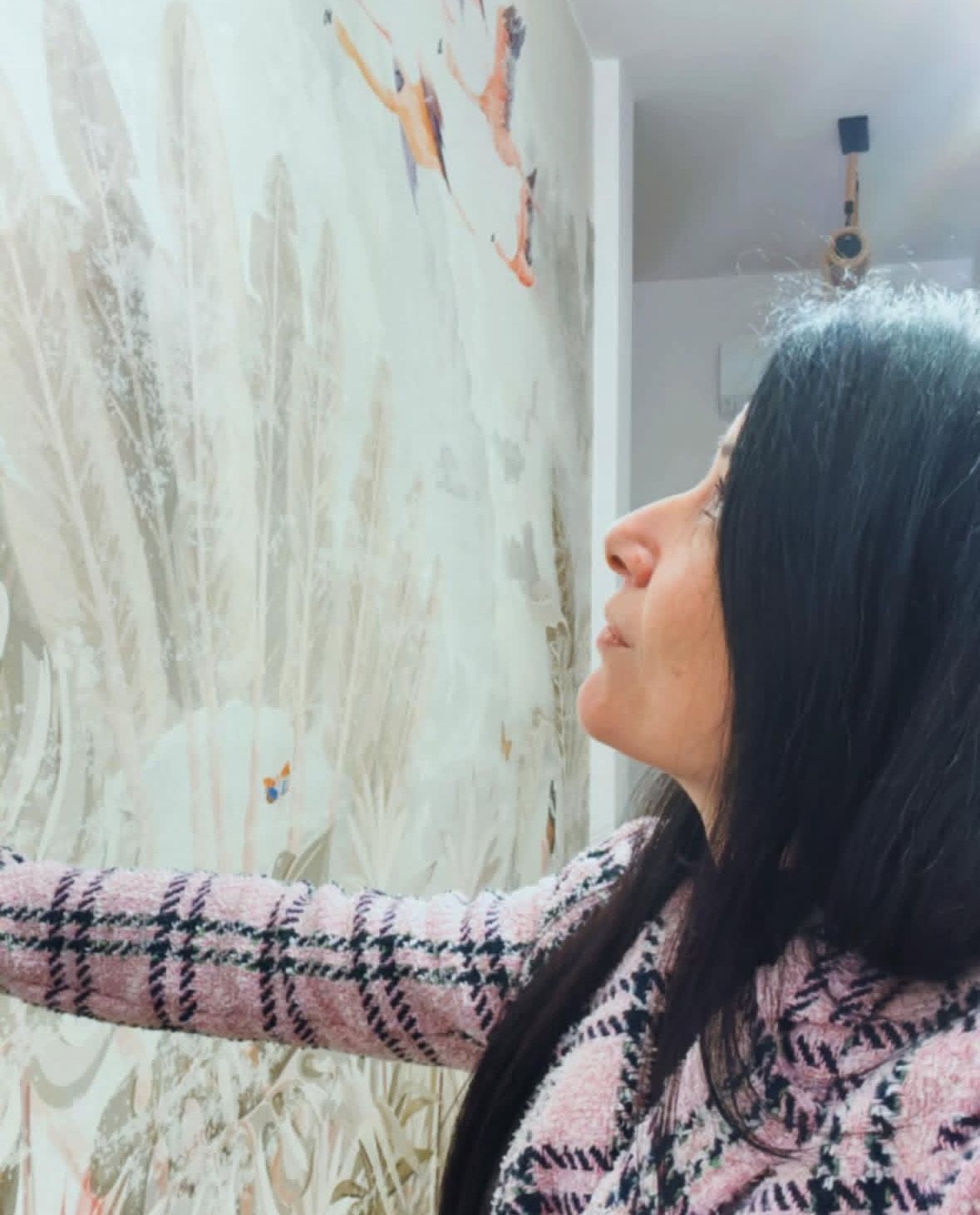 Una persona con un abito a fantasia e stivali è in piedi con le braccia incrociate in un ufficio con scaffali e sedie marroni.