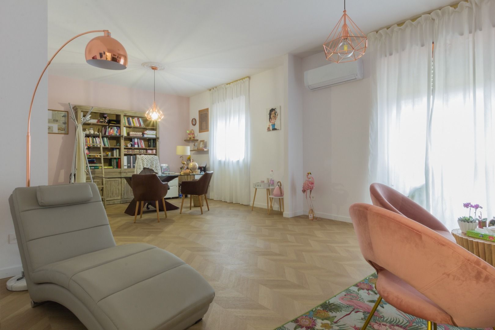 Un soggiorno con chaise longue beige, un set da pranzo e una zona scrivania con mensole, caratterizzato da pavimenti in legno chiaro.