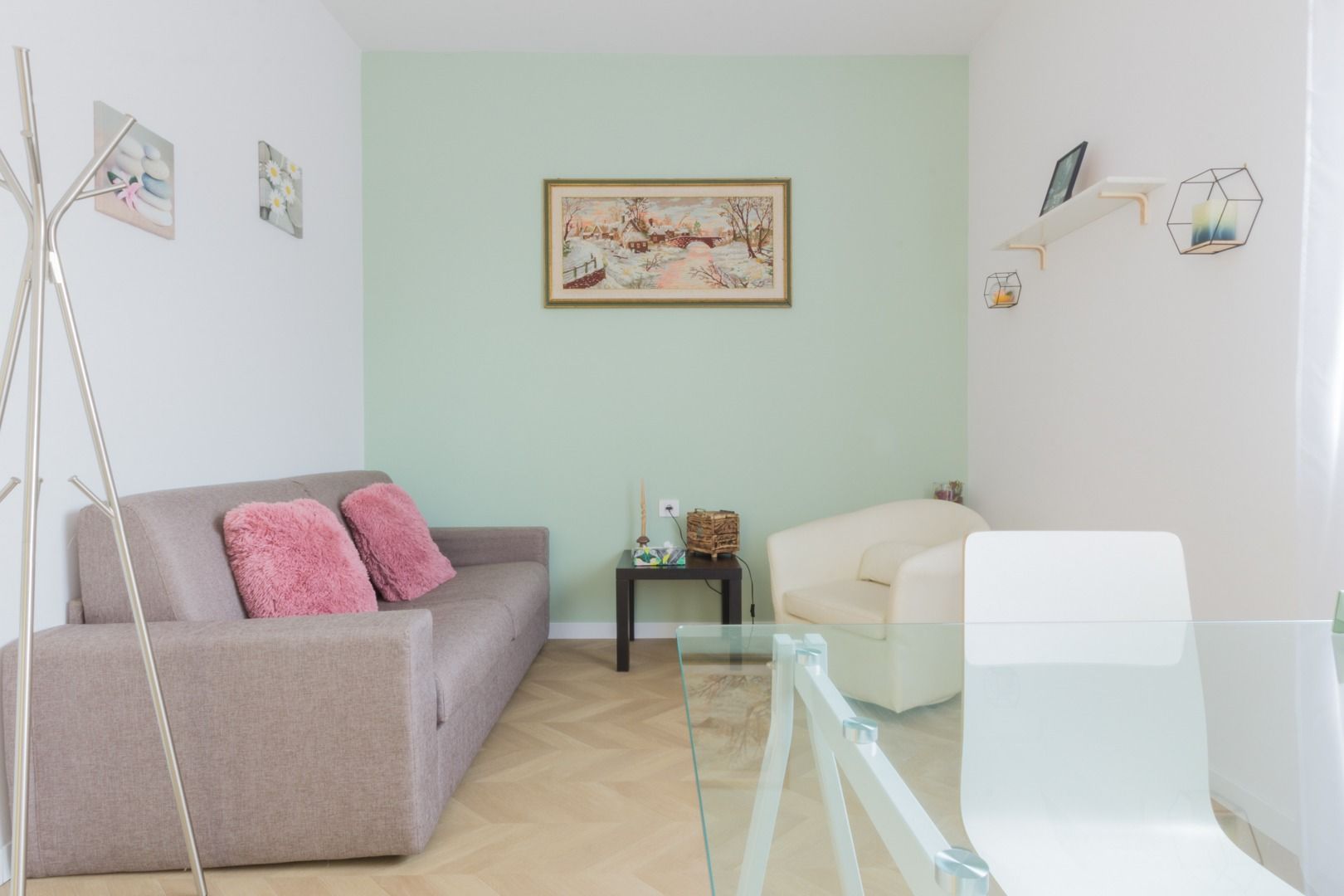 Un soggiorno con un divano beige, due cuscini rosa, una poltrona bianca, un quadro paesaggistico incorniciato e un tavolino.