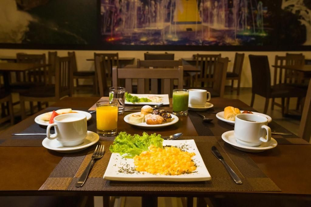 Mesa de café da manhã posta com ovos mexidos, bebidas e doces em um ambiente de restaurante.