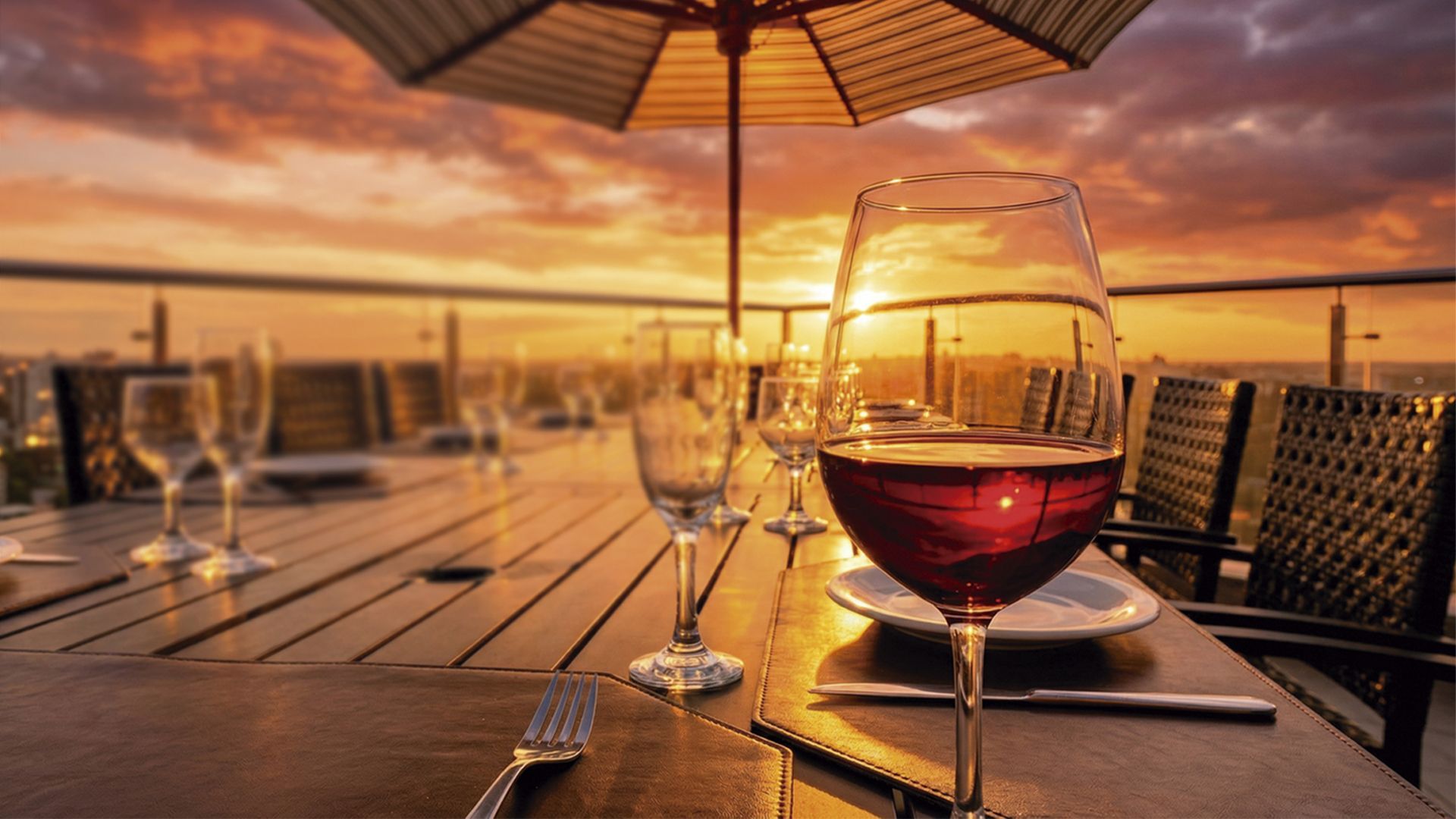 Uma taça de vinho tinto numa mesa posta num pátio com vista para uma paisagem urbana deslumbrante ao pôr do sol.
