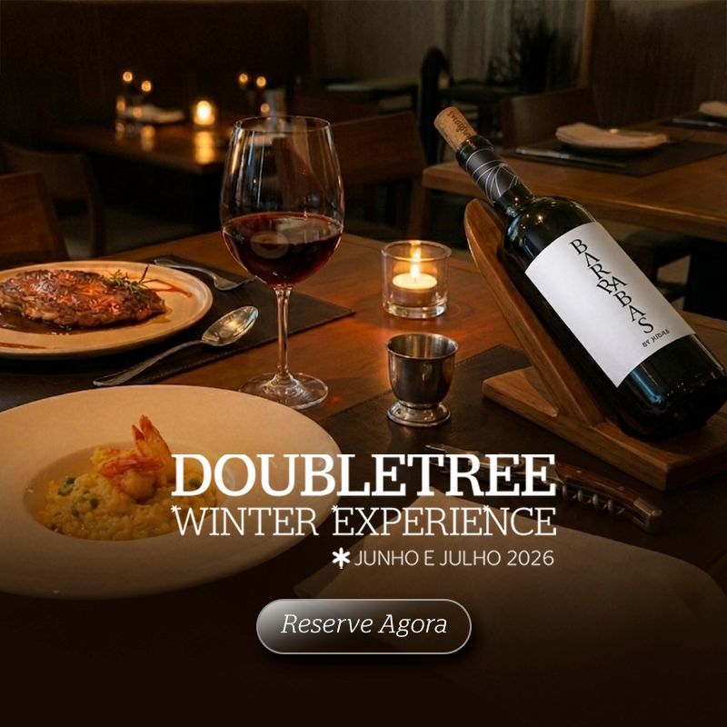 Jantar elegante à luz de velas com vinho e pratos servidos individualmente, promovendo a Experiência de Inverno DoubleTree e o programa “Reserve Agora”.
