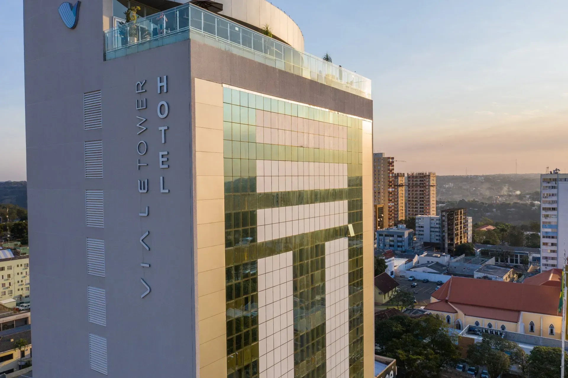 Edifício alto e moderno de hotel em meio à paisagem urbana. "Hotel" em texto vertical na lateral, fachada de vidro refletivo.