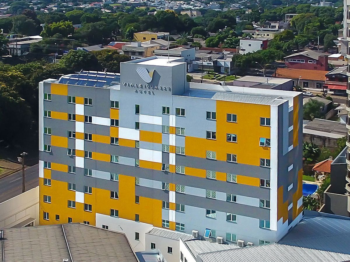Vista aérea de um edifício hoteleiro de vários andares com uma fachada que apresenta um padrão geométrico em amarelo, cinza e branco.