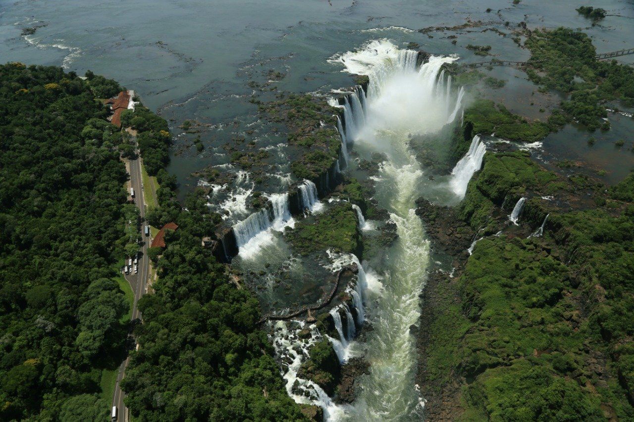 Vista aérea das Cataratas do Iguaçu, Argentina. A água cai em cascatas sobre vários níveis de queda d'água, cercada por uma vegetação verdejante.