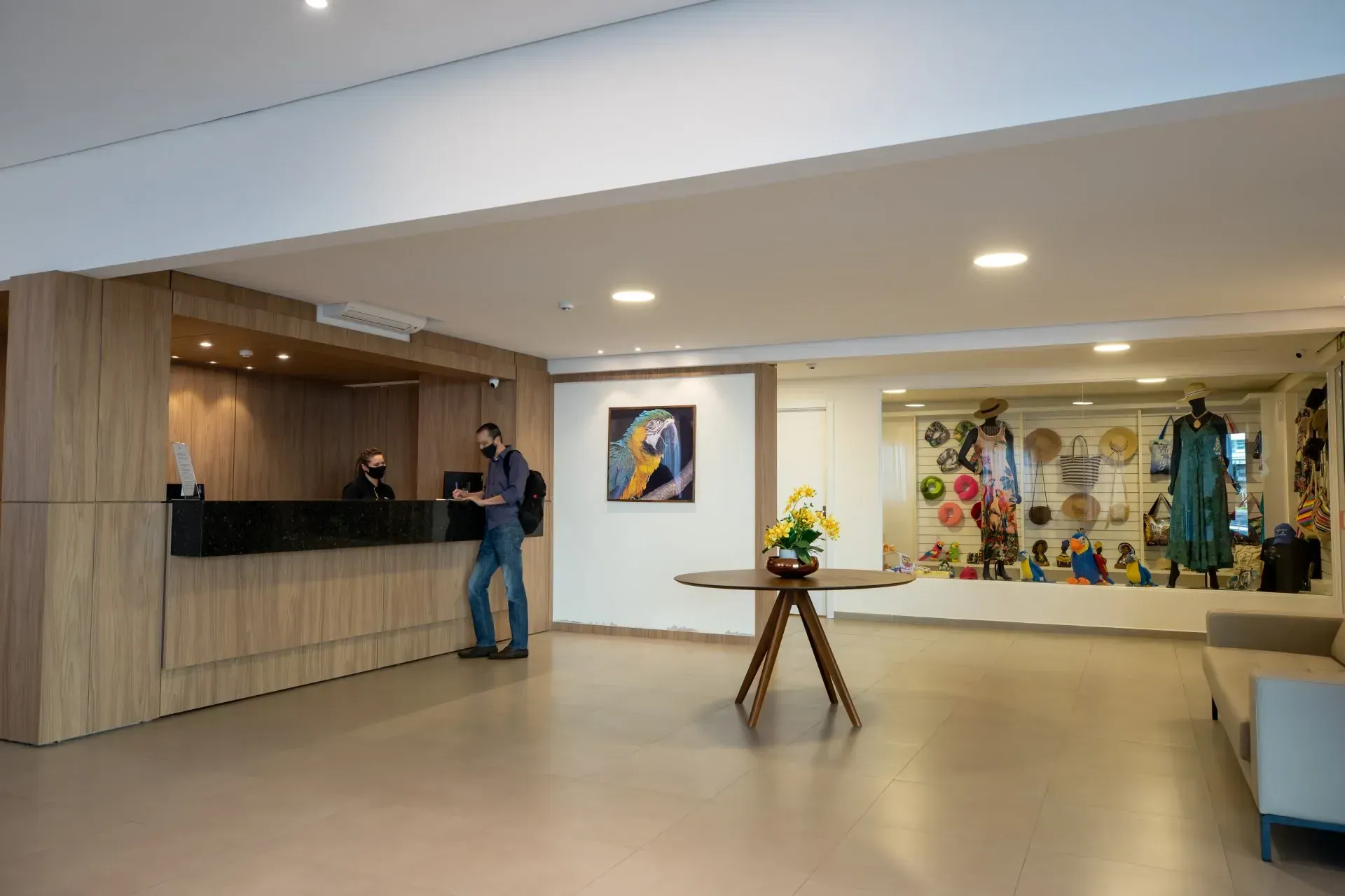 Saguão do hotel com recepção, hóspedes, exposição de itens, arte e assentos.