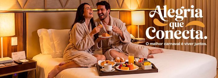 Couple in robes enjoying breakfast in bed. Smiling, laughing. Luxury hotel room, soft lighting.