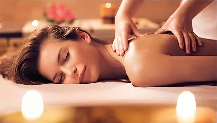 Mulher recebendo uma massagem nas costas em um spa; velas e iluminação suave.