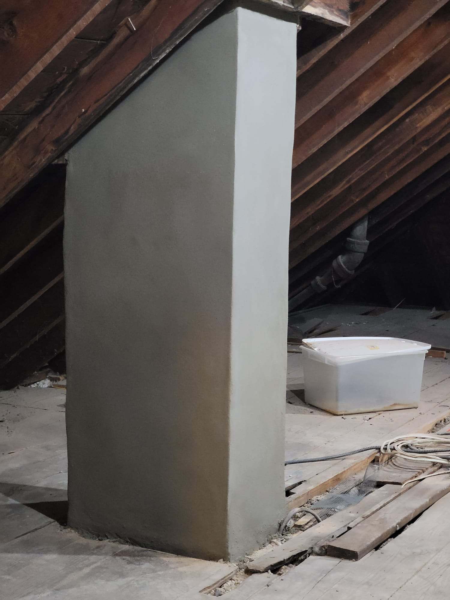 A white box is sitting on the floor next to a pillar in an attic.
