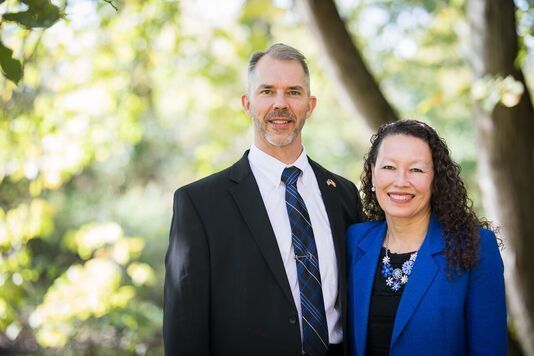 A man and a woman are standing next to each other in front of a tree.