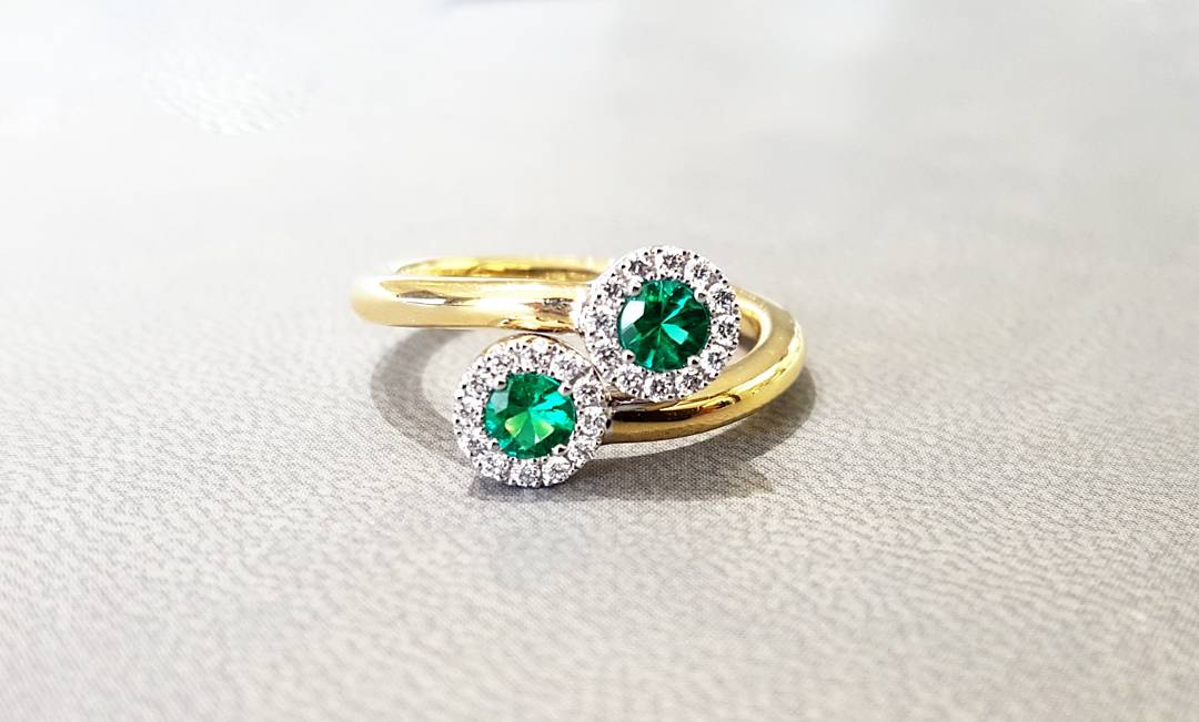 A close up of a gold ring with emeralds and diamonds on a table.
