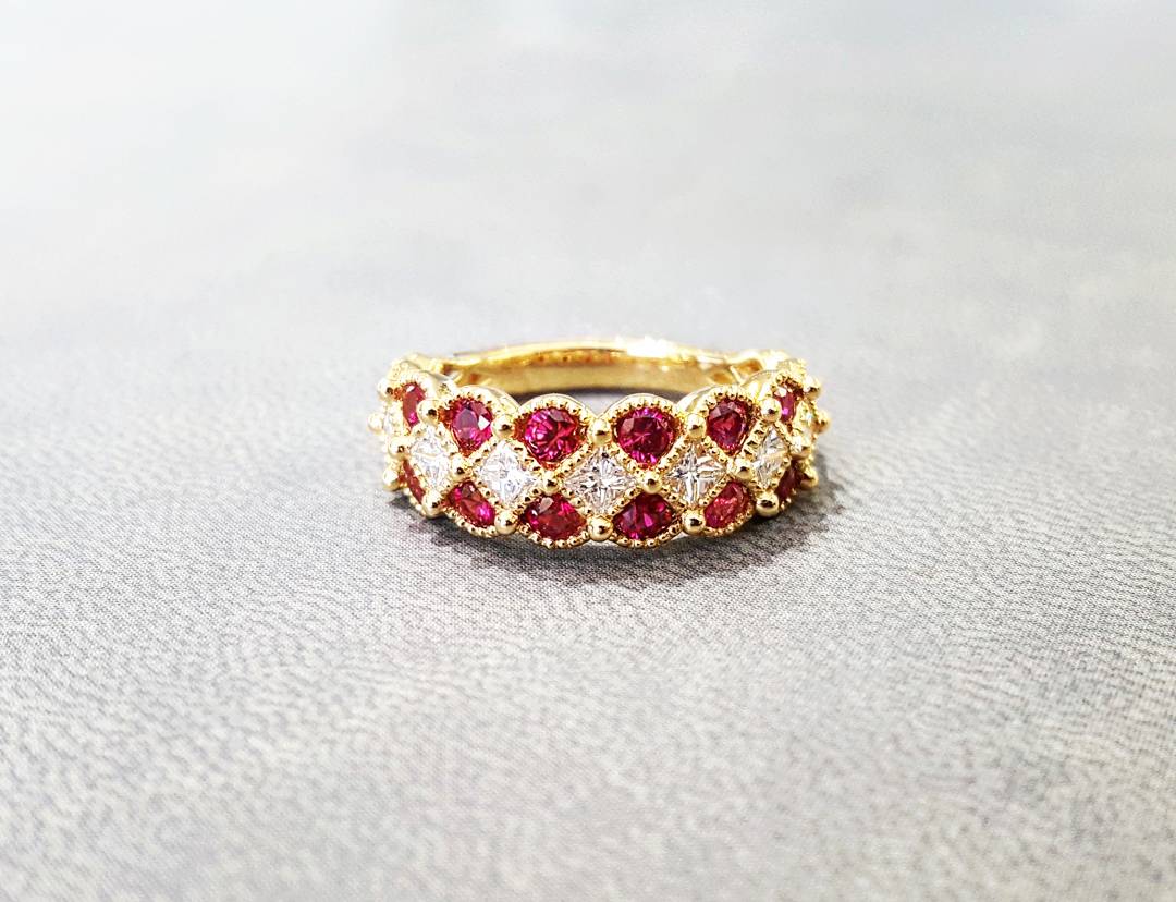 A close up of a gold ring with ruby and diamond stones on a table.