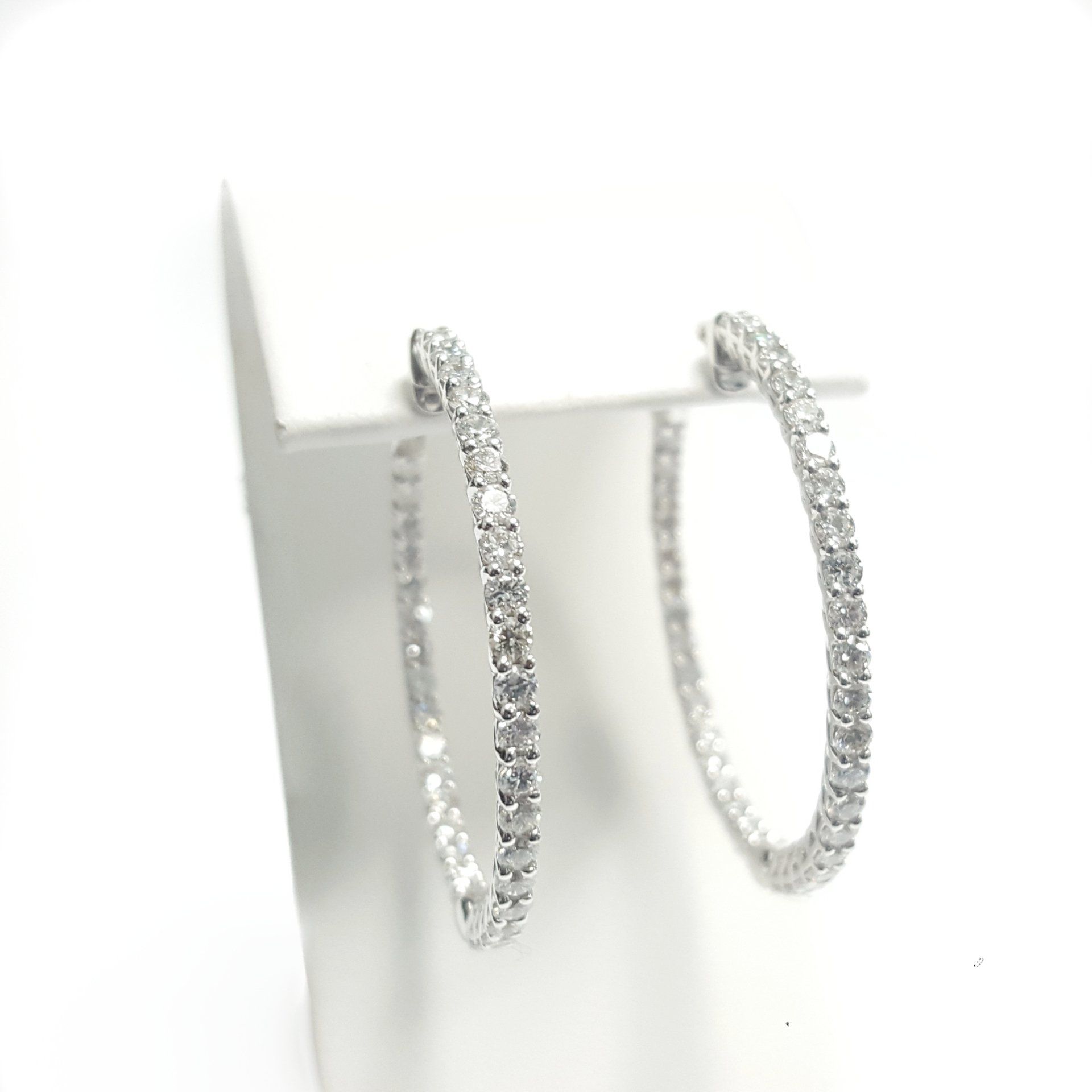 A pair of diamond hoop earrings are sitting on a white surface.