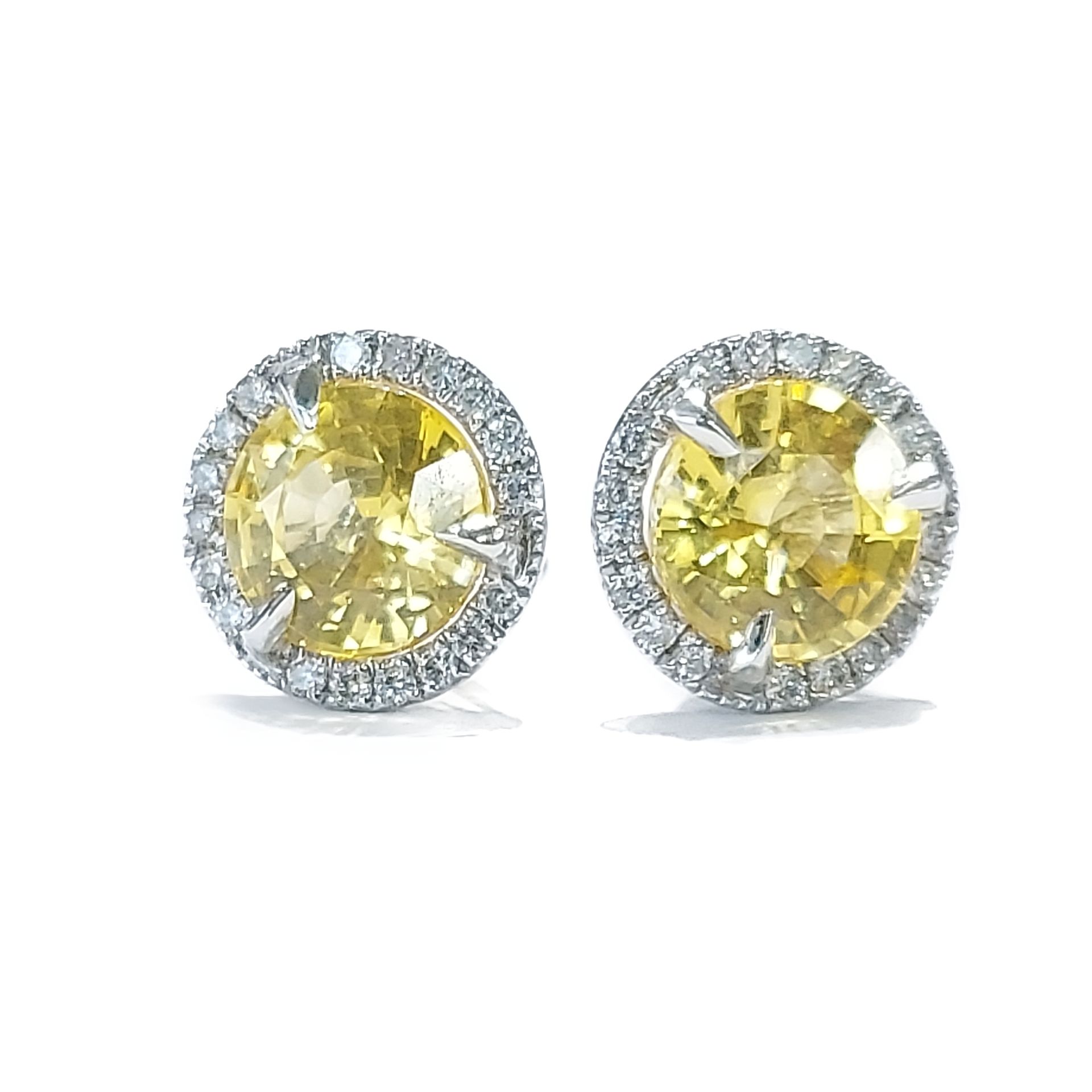 A pair of yellow sapphire and diamond stud earrings on a white background.