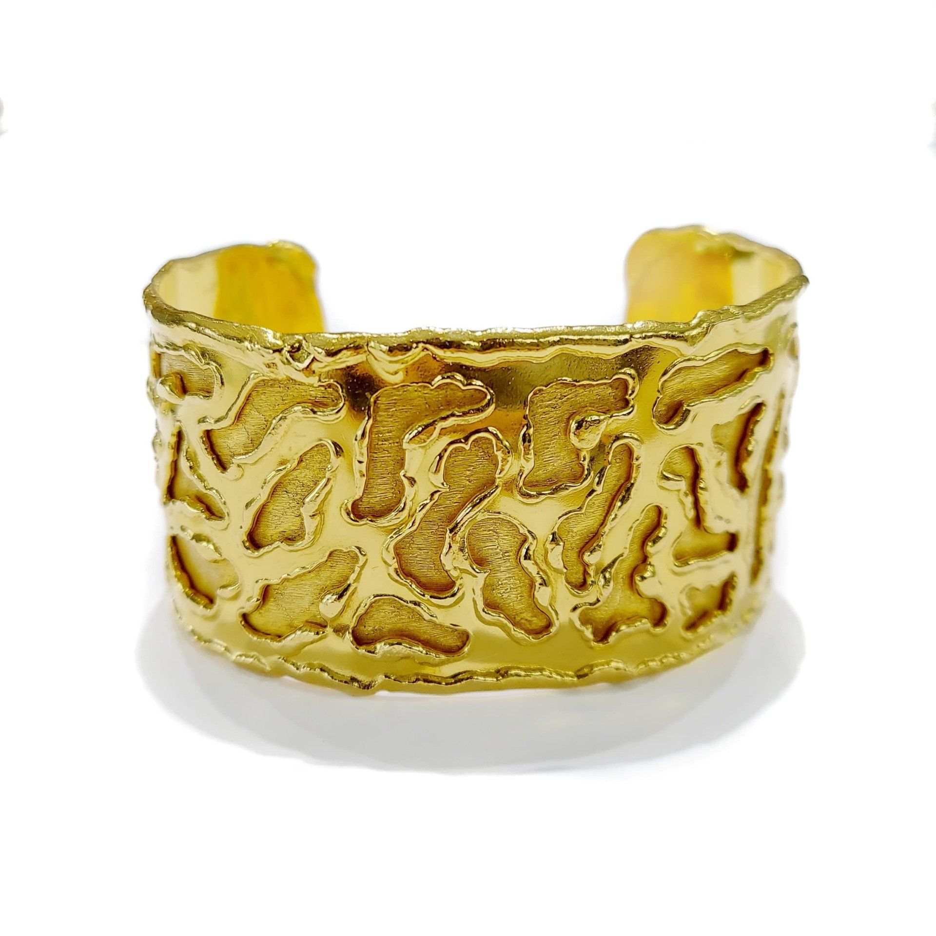 A gold bracelet with a pattern on it is on a white surface.