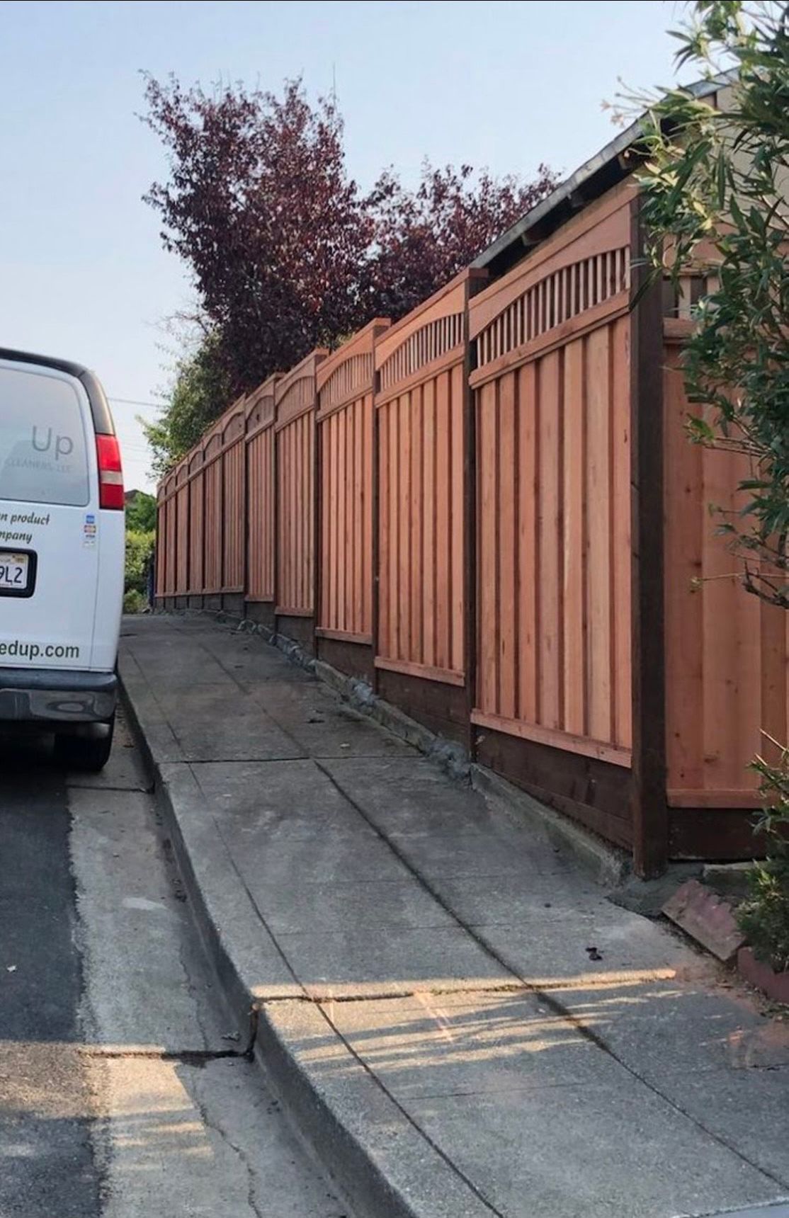 A white van is parked on the side of the road next to a wooden fence.