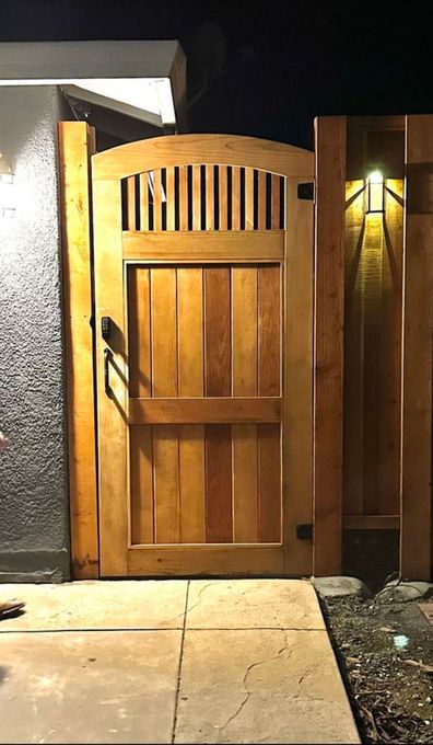 A wooden gate is sitting next to a fence in front of a building at night.