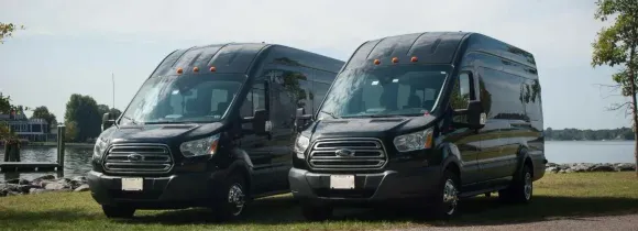 Two black vans parked on a grassy area, with a lake and trees in the background.