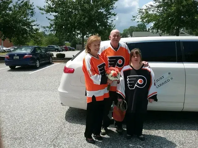 Three people in Flyers jerseys pose near a white limousine in a parking lot.