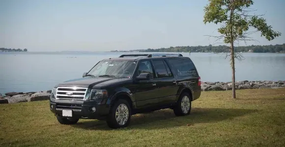 Black sedan parked on grassy bank overlooking a lake.