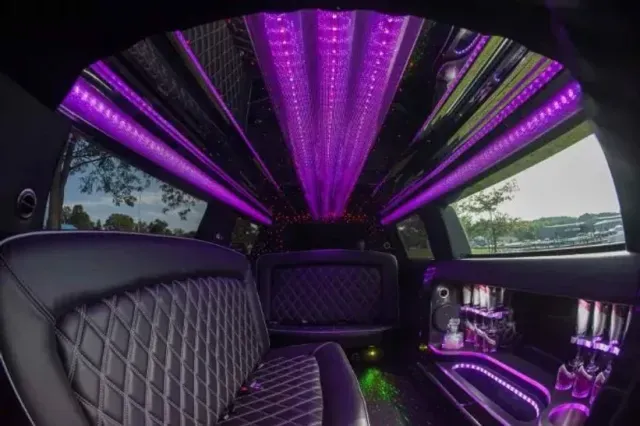 Interior of a black limousine with purple neon lighting. Black quilted seats and bar area visible.