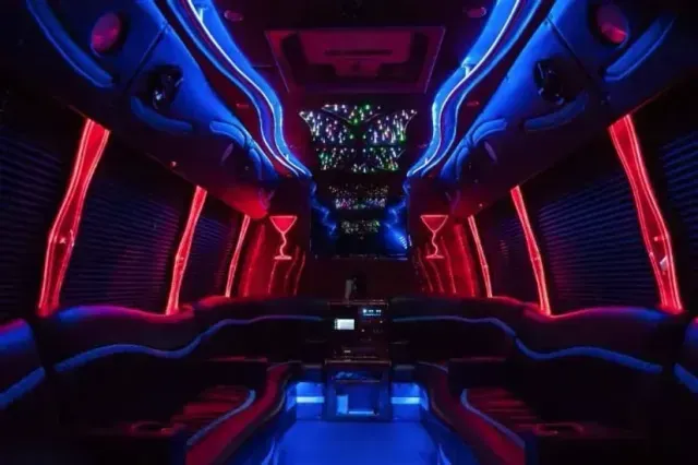 Inside of a party bus with blue and red neon lighting, black seats, and a bar area.