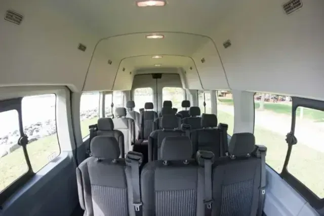 Interior view of a white passenger van with rows of grey seats and windows.