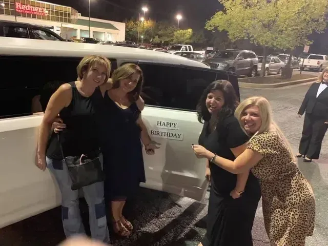 Four women pose by a white limo with 