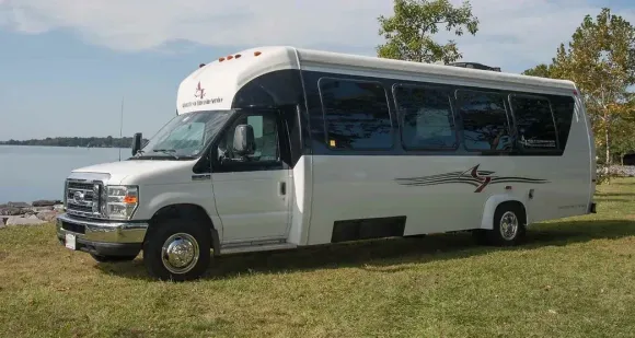 White passenger bus parked on grass near a body of water on a sunny day.
