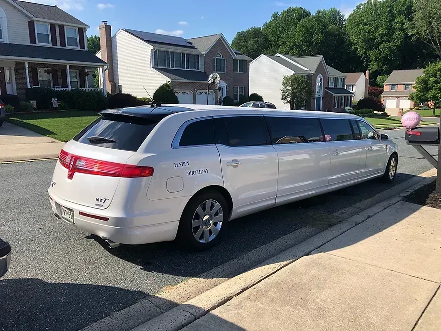 White limousine parked on a residential street, houses in the background, sunny day.