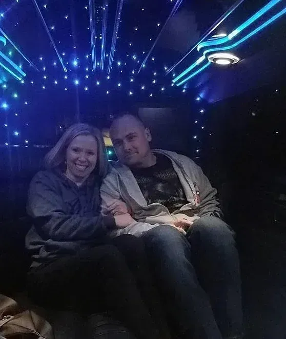 Couple smiling, holding hands inside a limo with starry ceiling and blue lights.