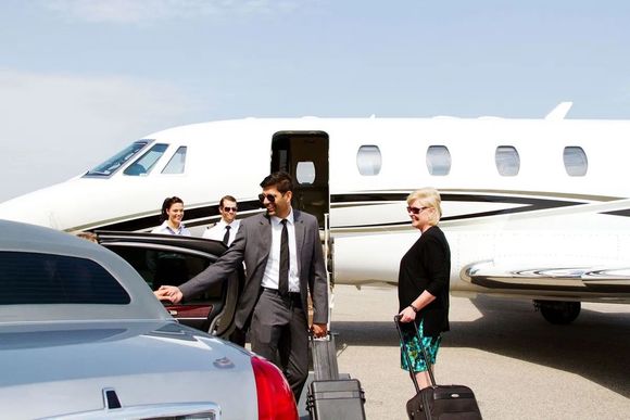 People exiting a private jet with luggage and a car waiting, outdoors.