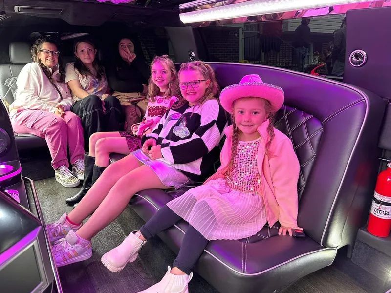 Six girls smiling in a black limousine with pink lights.