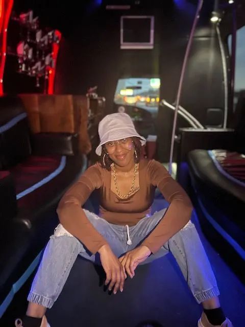 Woman in brown top, jeans, and bucket hat sits in a limousine.