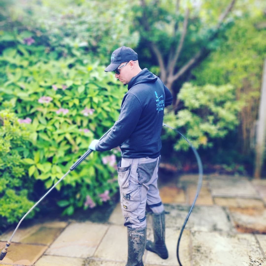A man is using a high pressure washer to clean a patio