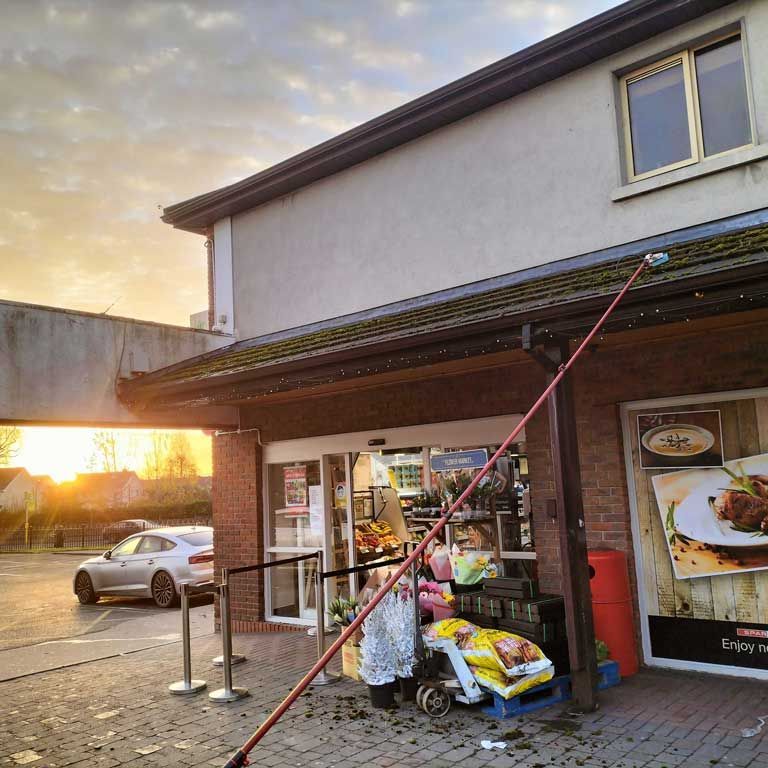 A man is cleaning the roof of a building with a long pole.