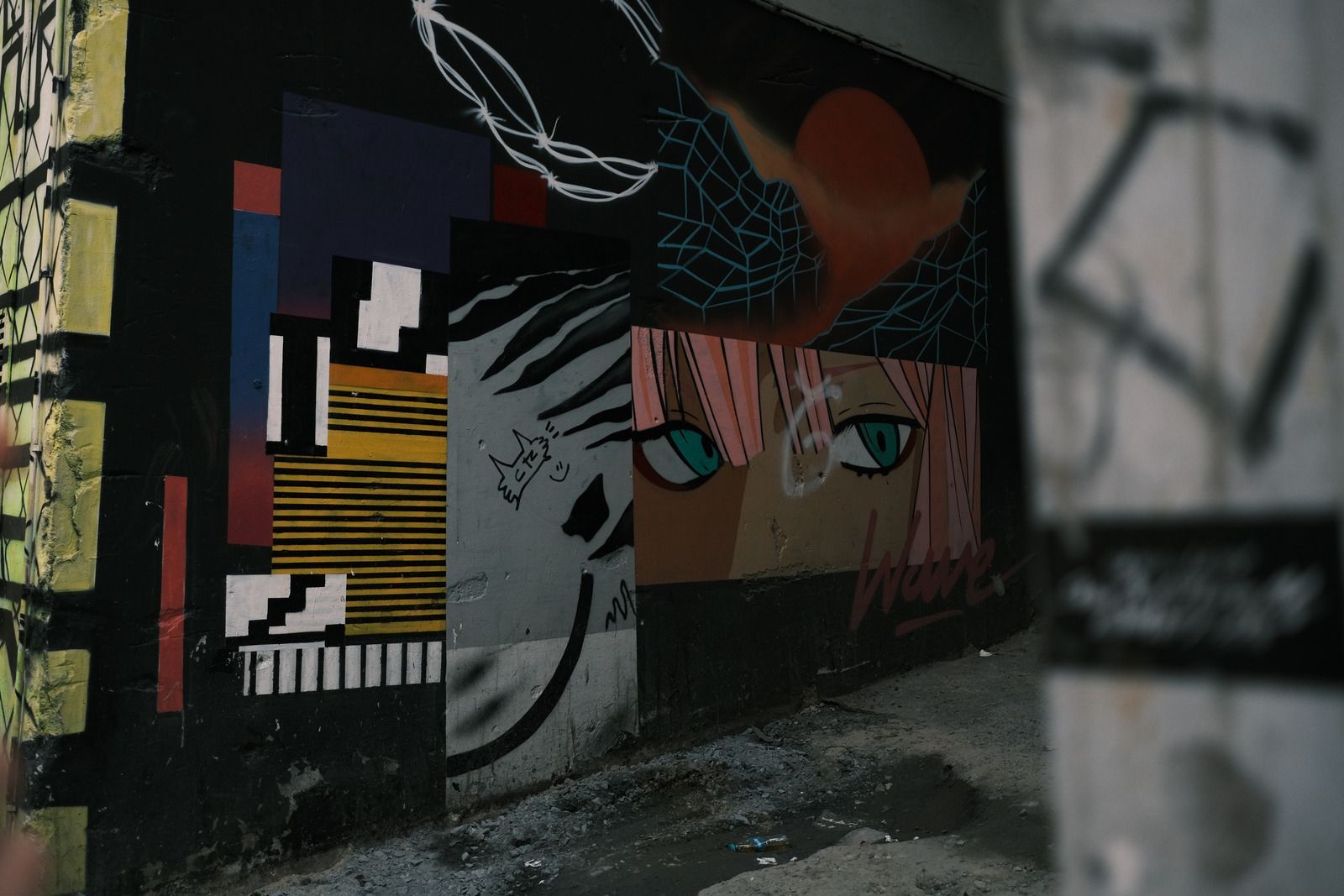 Graffiti art on a dark wall: faces, geometric shapes, and colorful designs in an alleyway.